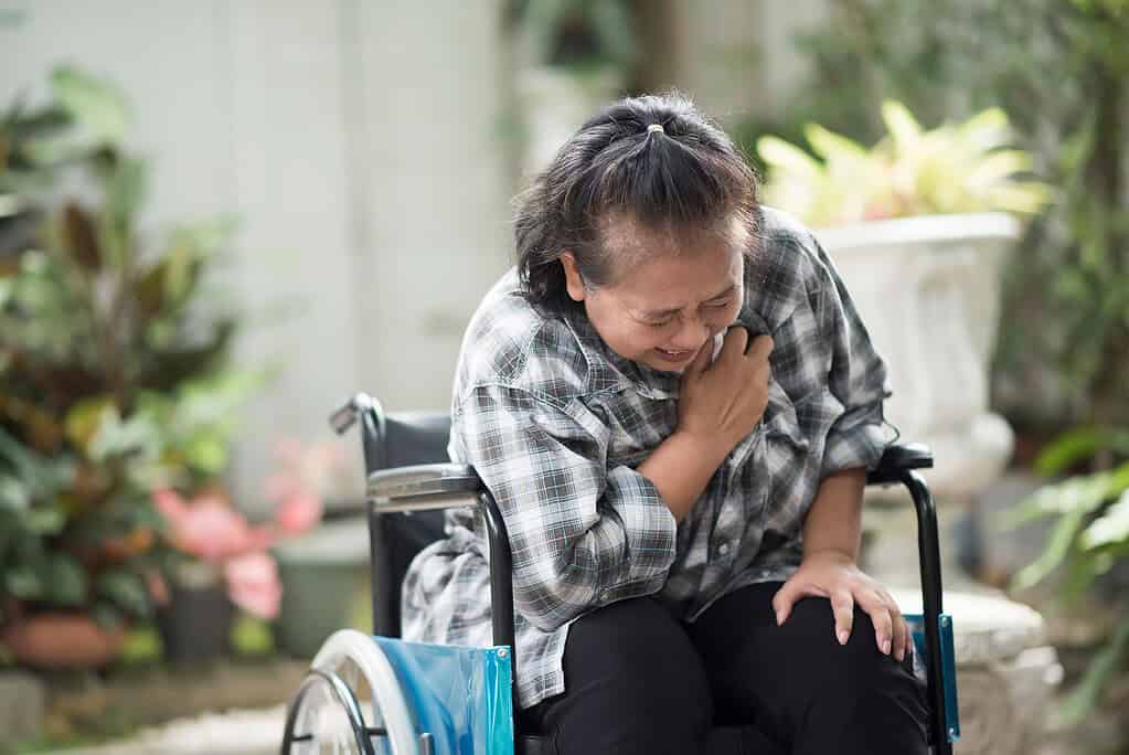 elderly woman sitting in a wheelchair clutching her chest in pain