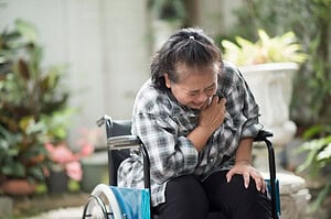 elderly woman sitting in a wheelchair clutching her chest in pain