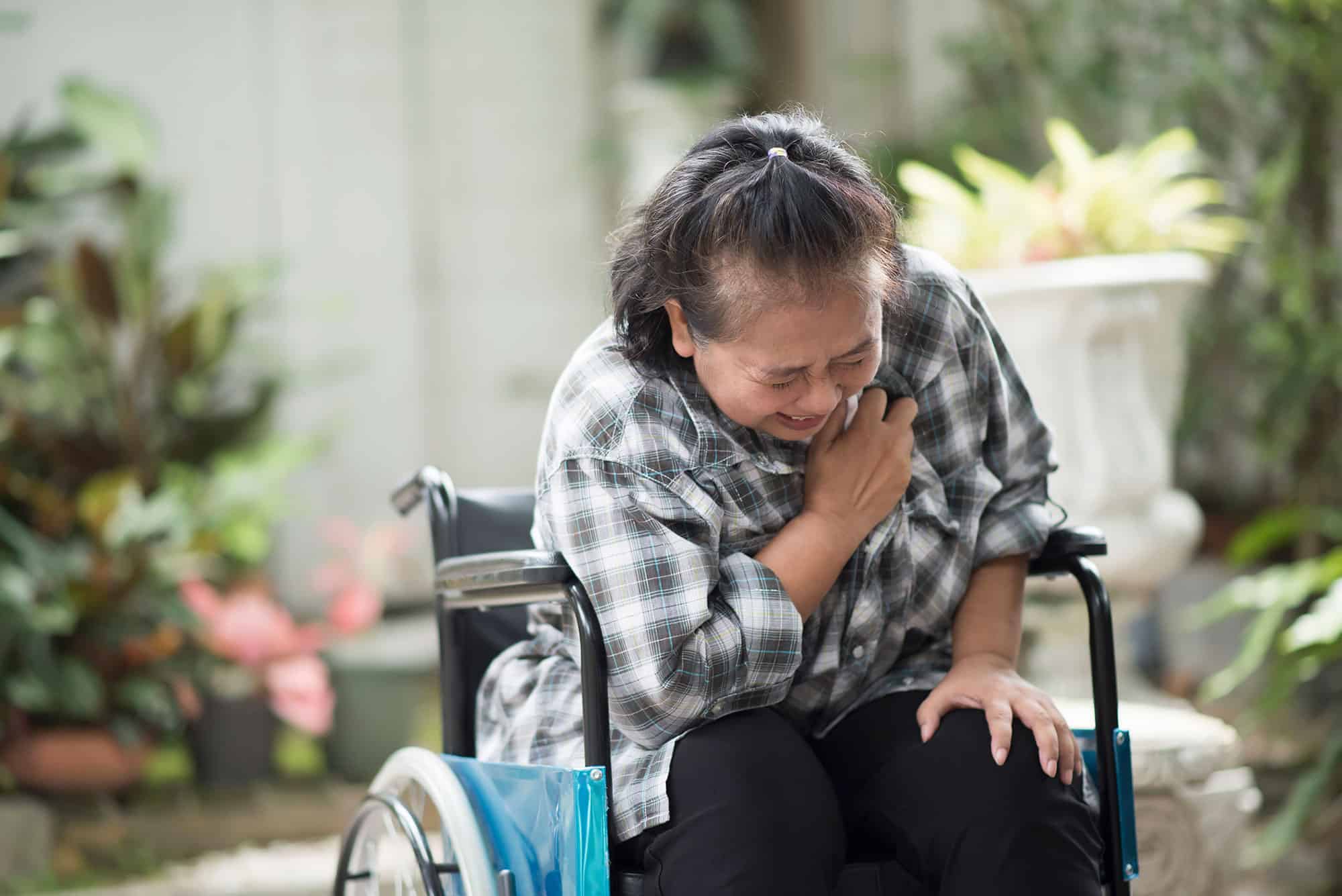 elderly woman sitting in a wheelchair clutching her chest in pain
